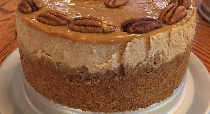 Pumpkin cheesecake topped with caramel and pecans on a white cake stand