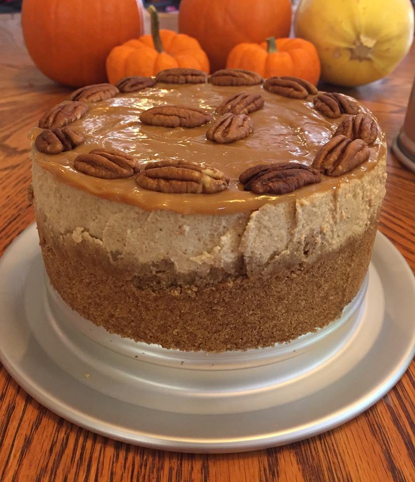 Pumpkin cheesecake topped with caramel and pecans on a white cake stand